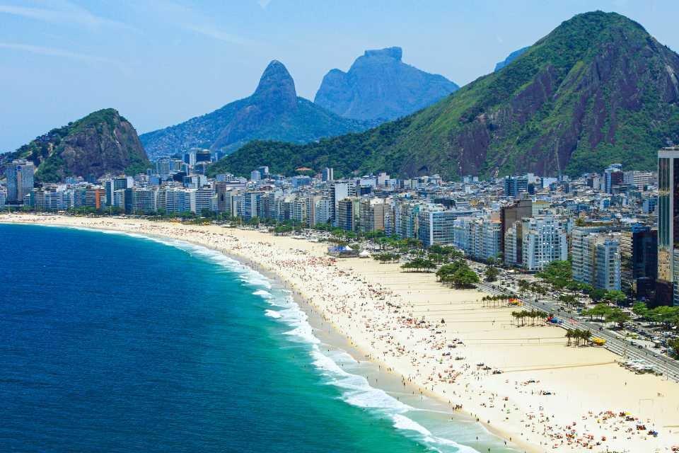 <h3>PRAIA DE COPACABANA</h3>A Praia de Copacabana é uma das praias mais famosas e vibrantes do Rio de Janeiro, estendendo-se por quase 4 quilômetros ao longo do Oceano Atlântico. Conhecida por seu formato curvo icônico e pelo movimentado calçadão, oferece uma mistura de banhos de sol, esportes de praia e entretenimento animado dia e noite. A praia é ladeada por quiosques que servem bebidas geladas e petiscos, enquanto os frequentadores podem desfrutar de atividades como vôlei, futebol de praia e surfe. Copacabana também é um centro cultural, sediando as celebrações de Réveillon com fogos de artifício espetaculares e as tradicionais festas de rua do Carnaval. Sua atmosfera animada e vistas deslumbrantes fazem dela um destino imperdível para turistas e locais.