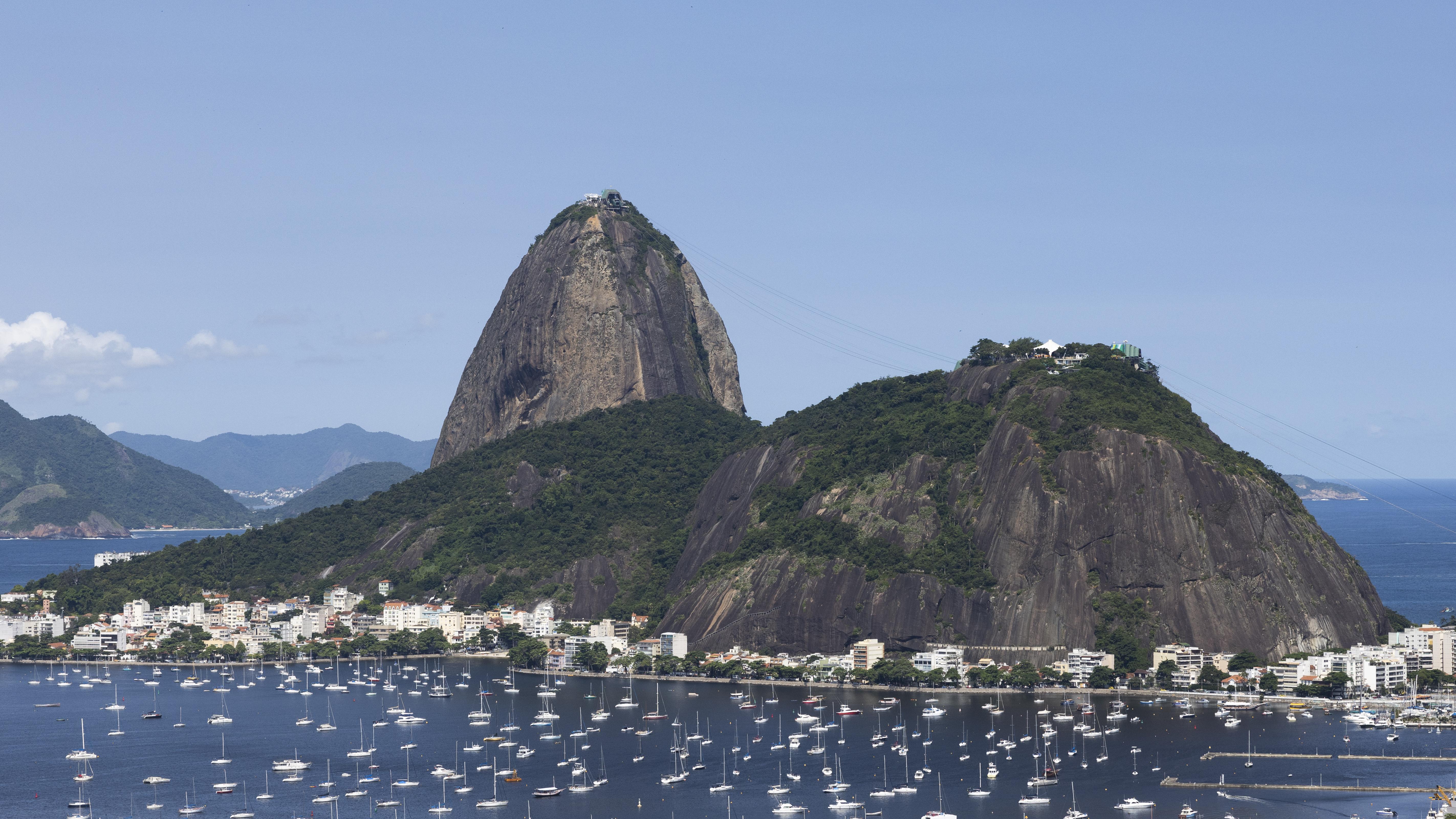 <h3>PÃO DE AÇÚCAR</h3>O Pão de Açúcar é um marco icônico do Rio de Janeiro, elevando-se 396 metros acima da Baía de Guanabara. Acessível por meio de um passeio de teleférico em duas etapas, os visitantes são brindados com vistas panorâmicas deslumbrantes da cidade, incluindo a Praia de Copacabana, o Cristo Redentor e as montanhas e ilhas ao redor. A montanha é composta de granito e quartzo, oferecendo trilhas para caminhadas e rotas de escalada para os entusiastas de atividades ao ar livre. No cume, os visitantes podem relaxar em cafés e apreciar a paisagem ou capturar fotos memoráveis do horizonte do Rio contra o pano de fundo do Oceano Atlântico.