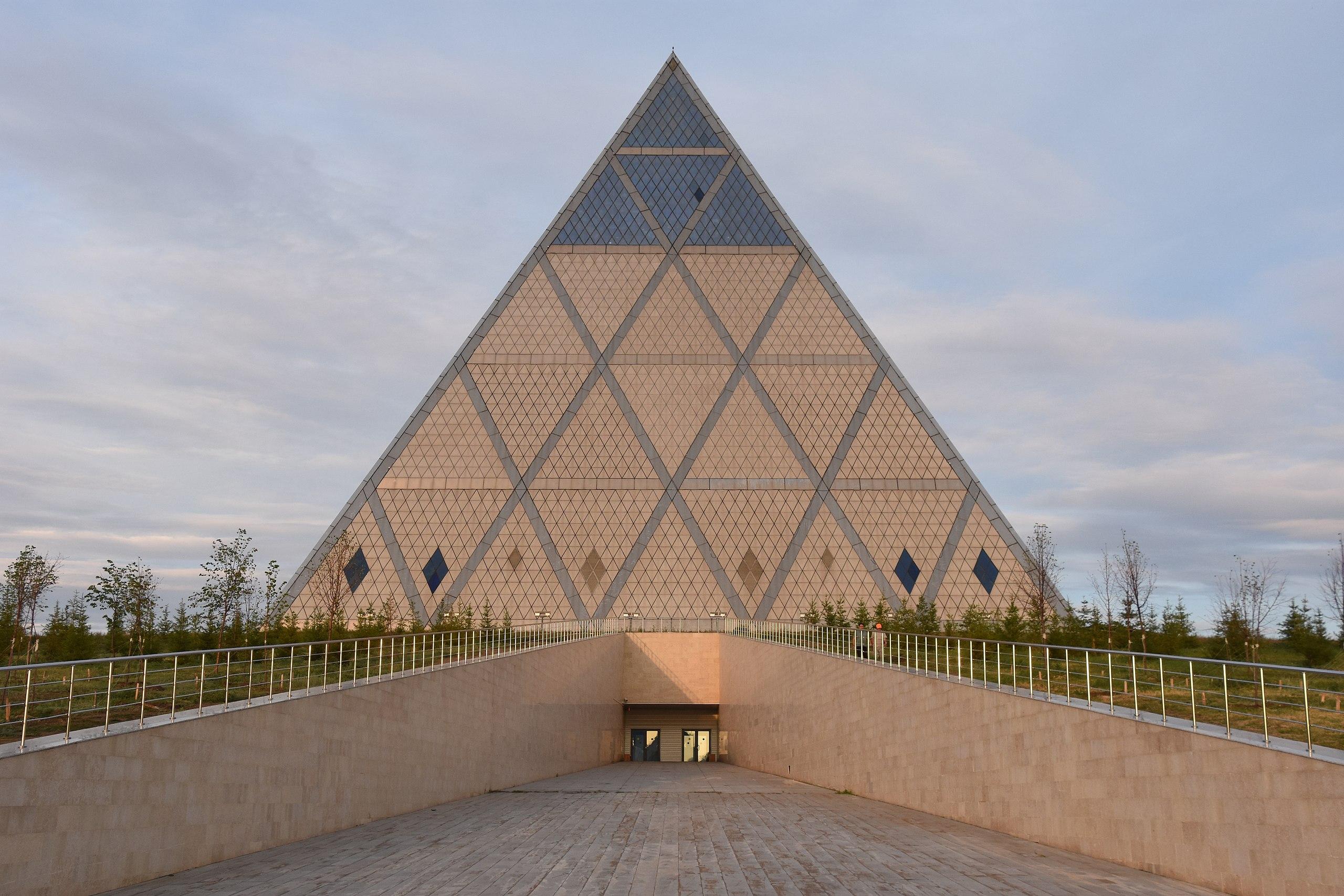 <h3>PALACE OF PEACE AND RECONCILIATION</h3>The Palace of Peace and Reconciliation, located in Nur-Sultan, Kazakhstan, is an architectural marvel designed by the renowned British architect Norman Foster. Completed in 2006, this striking pyramid-shaped structure stands 62 meters tall and is characterized by its glass apex, which serves as a symbol of openness and transparency. The palace was constructed to promote global peace and understanding among different cultures and religions, hosting international conferences, meetings, and cultural events aimed at fostering dialogue and cooperation. Inside, the building features a 1,500-seat opera house, exhibition spaces, and an atrium with a stained glass ceiling representing a dove of peace. The Palace of Peace and Reconciliation stands as a testament to Kazakhstan's commitment to peace and diplomacy on the global stage, while its unique design has made it a prominent symbol of Nur-Sultan's modern architectural landscape.